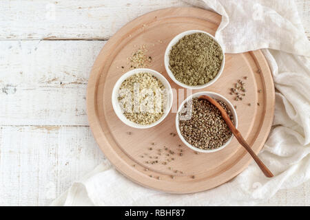 Organico tutta canapa semi, semi mondati e proteine in polvere in recipienti su un bianco sullo sfondo di legno, flatlay Foto Stock