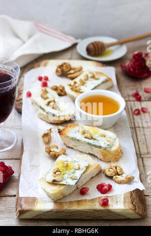 Panini con formaggio blu, melograno, miele e noci servita con vino rosso. In stile rustico, il fuoco selettivo. Foto Stock