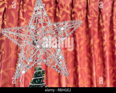 Silver Star di metallo su un albero di Natale contro un sipario rosso sfondo Foto Stock