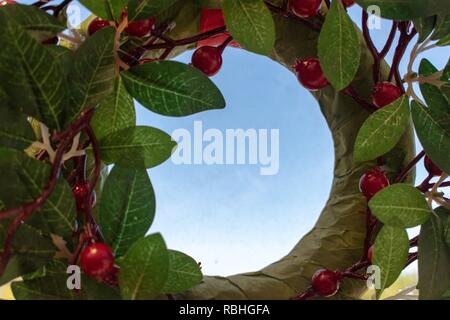 Round incorniciato Natale Holly con blu cielo copyspace in medio Foto Stock