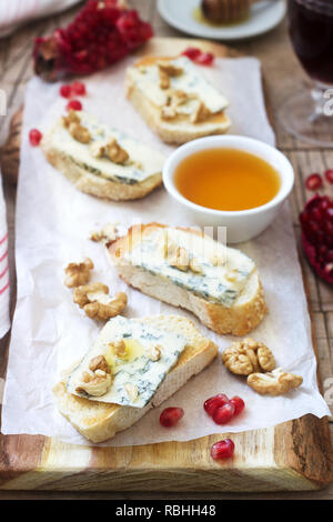 Panini con formaggio blu, melograno, miele e noci servita con vino rosso. In stile rustico, il fuoco selettivo. Foto Stock