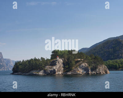 Un giorno di crociera del fiordo Lysefjorden in oriente di Stavanger, Norvegia, piccola isola nel fiordo con un faro e alberi Foto Stock