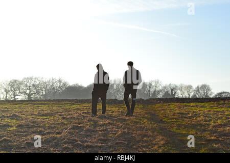 Sagome di due giovani uomini a piedi in un campo in North Downs vicino Shoreham, Kent, su un croccante di inverno di giorno. Potrebbero essere i lavoratori agricoli, ramblers