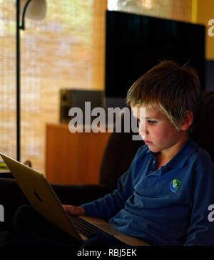 Un bambino di sei anni ragazzo indossa uniformi scolastiche lavorando su un computer portatile Foto Stock