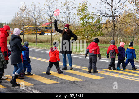 Un ridere maestra d'asilo tenendo premuto fino a 'Stop' firmare mentre i suoi allievi attraversare la strada. Foto scattata in Quebec in modo che il segnale di stop legge Arret. Foto Stock