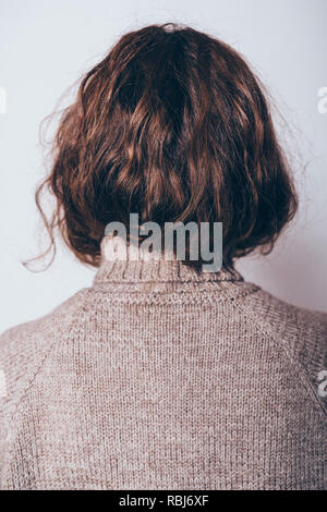 Vista posteriore della giovane donna con capelli ricci vestito di lana maglione turtleneck, close-up. Foto Stock