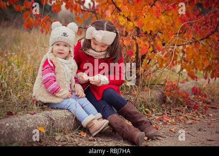 Moda baby ragazze sorelle elegante vestito brunnette e biondo indossando autunno caldo abbigliamento giacche in posa felici insieme in un colorato fogliame.F Foto Stock