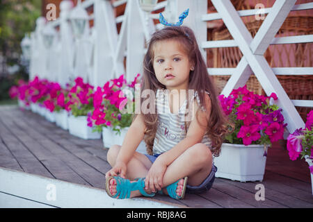 Bellissima ed elegante simpatico baby girl Brunette con capelli in posa su legno giardino pieno di fiori che indossa jeans minuscole magliette e ariosa skivy underwaist e b Foto Stock