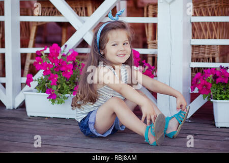 Bellissima ed elegante simpatico baby girl Brunette con capelli in posa su legno giardino pieno di fiori che indossa jeans minuscole magliette e ariosa skivy underwaist e b Foto Stock