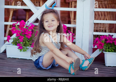 Bellissima ed elegante simpatico baby girl Brunette con capelli in posa su legno giardino pieno di fiori che indossa jeans minuscole magliette e ariosa skivy underwaist e b Foto Stock