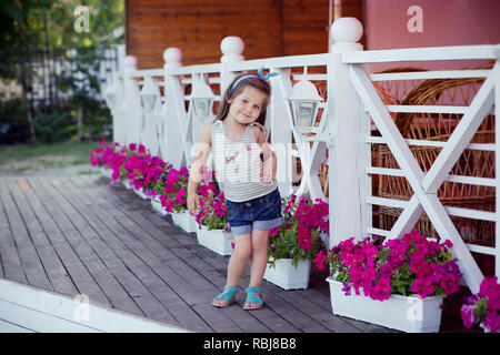 Bellissima ed elegante simpatico baby girl Brunette con capelli in posa su legno giardino pieno di fiori che indossa jeans minuscole magliette e ariosa skivy underwaist e b Foto Stock