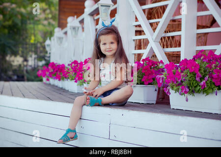 Bellissima ed elegante simpatico baby girl Brunette con capelli in posa su legno giardino pieno di fiori che indossa jeans minuscole magliette e ariosa skivy underwaist e b Foto Stock