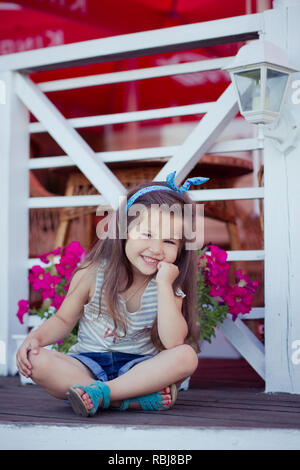 Bellissima ed elegante simpatico baby girl Brunette con capelli in posa su legno giardino pieno di fiori che indossa jeans minuscole magliette e ariosa skivy underwaist e b Foto Stock