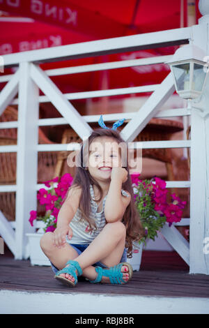 Bellissima ed elegante simpatico baby girl Brunette con capelli in posa su legno giardino pieno di fiori che indossa jeans minuscole magliette e ariosa skivy underwaist e b Foto Stock