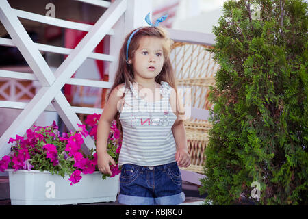 Bellissima ed elegante simpatico baby girl Brunette con capelli in posa su legno giardino pieno di fiori che indossa jeans minuscole magliette e ariosa skivy underwaist e b Foto Stock