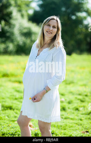 Donna incinta mentre tiene il suo ventre e sorridente Foto Stock