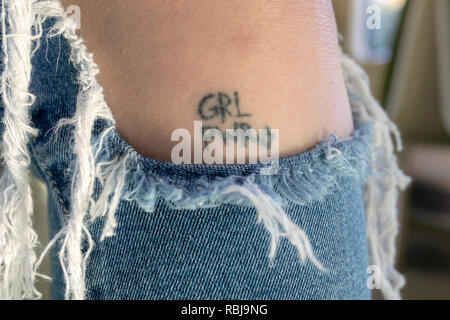Una giovane donna che indossa jeans strappati mostrare un 'Girl Power' tatuaggio sulla sua gamba. Foto Stock