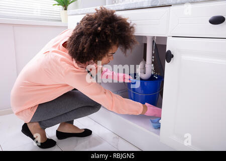 Close-up di una giovane donna di immissione della benna blu sotto l'acqua perde dal tubo del dissipatore Foto Stock