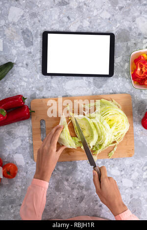 Donna di mano cavolo di taglio in prossimità della tavoletta digitale con schermo bianco sul banco di cucina Foto Stock