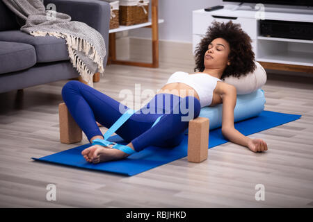 Rilassata giovane donna giacente sul tappetino Fitness Ginnastica con cinghia di Yoga e due blocchi Foto Stock