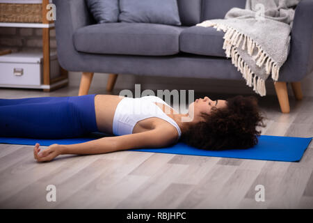 Atletica Giovane donna sdraiata su Blu materassino yoga su pavimento in legno duro Foto Stock