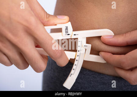 Close-up di una donna sottile utilizzando Fat calibro per misurare il grasso corporeo sulla linea di cintura Foto Stock