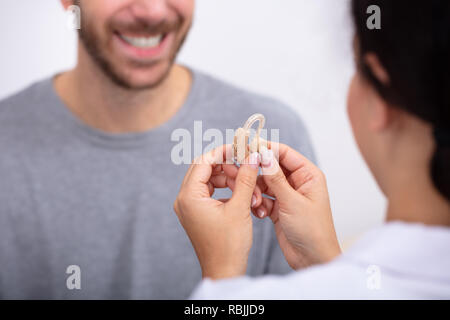 Giovane maschio alla ricerca del paziente al medico donna Holding Hearing Aid in clinica Foto Stock