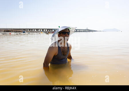 Un uomo che indossa e occhiali da sole a ombrello hat nel lago di Urmia, West Azerbaijan provincia, Iran Foto Stock