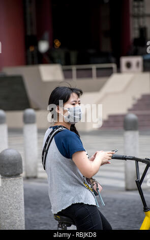 Ciclista femminile in Cina a Shanghai, indossare una maschera per il viso Foto Stock