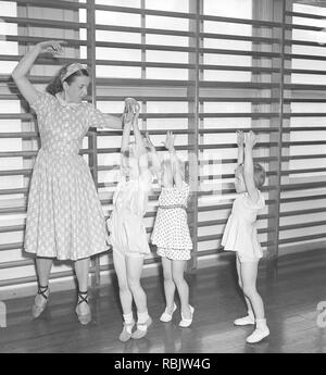 Ginnastica in 1940s. Un insegnante di donne nella palestra della scuola è che mostra come spostare e danza. Tre bambini in età diverse cerca di seguire il suo piombo. Foto Kristoffersson Ref AB22-12. La Svezia 1940s Foto Stock