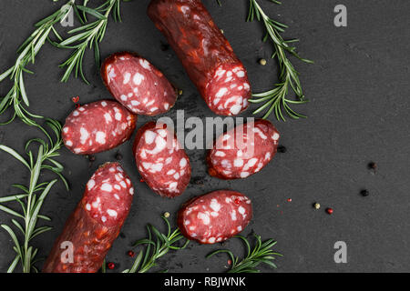 Salame affumicato su nero ardesia sfondo. Salsicce con rosmarino e pepe. vista superiore con spazio di copia Foto Stock