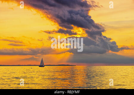 Un bel tramonto sul mare con una barca a vela e nuvole drammatico Foto Stock