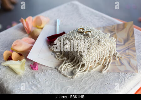 Una coppia di anelli di nozze su un cuscino bianco. La parte superiore del cuscino è realizzato con perline. Foto Stock