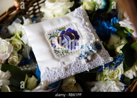 Una coppia di anelli di nozze su un cuscino bianco. Il cuscino è nel Cestino con fiori. Foto Stock