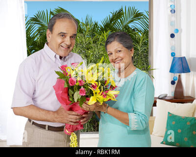 Il vecchio uomo di dare un mazzo di fiori a sua moglie nella loro casa Foto Stock