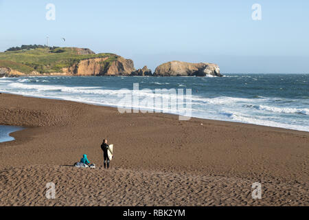 Un surfista si affaccia verso l'oceano al Rodeo Beach si trova a Fort Cronkhite nel Golden Gate National Recreation Area. Foto Stock