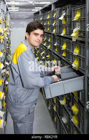 Lavoratore in magazzino tra lunghi scaffali con una varietà di scatole Foto Stock