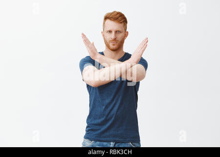 La mia casa mia, regole di alcol. Ritratto di grave-cercando coppia attraente redhead maschio con setola in blu t-shirt, facendo attraversare con le mani vicino al torace, mostra stop, abbastanza o gesto di rifiuto Foto Stock