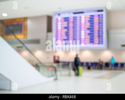 Sfocato l'orario di imbarco degli schermi del monitor e i passeggeri in aeroporto terminale hall area interna per arrivo il passeggero. Foto Stock