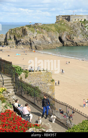 TENBY, Pembrokeshire, Galles - Agosto 2018: persone con cani parlando su parte della passeggiata che si affaccia su St Catherine's Island e Castle Beach in dieci Foto Stock