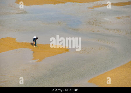 TENBY, Pembrokeshire, Galles - Agosto 2018: Persona su un sandbank in Tenby tagliati fuori dalla marea. Egli è di alzare i suoi pantaloni in fine di Wade Foto Stock