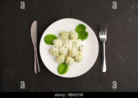 Piastra bianca di gnocchi con spinaci e formaggio con coltello e forchetta su sfondo grigio, piatto laico, vista aerea Foto Stock