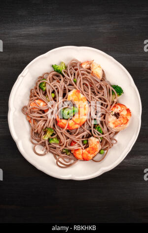 Un piatto di soba, Tagliatelle di grano saraceno con gamberi e verdure, ripresa dall'alto su uno sfondo nero con spazio di copia Foto Stock