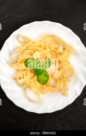 Un primo piano di un piatto di pasta italiana con parmigiano grattugiato e di foglie di basilico fresco, girato dalla parte superiore su uno sfondo nero con spazio di copia Foto Stock