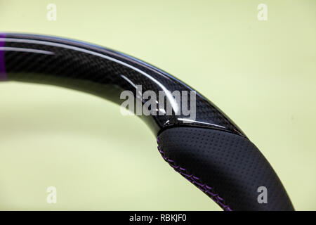 Close-up di un volante di sterzo dettaglio realizzato in fibra di carbonio nera con traforato in cuoio cucita con filo color porpora in un design e ottimizzazione per officina Foto Stock