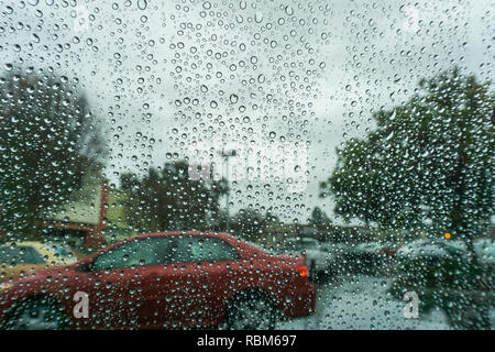 Le gocce di pioggia sul parabrezza in un giorno di pioggia, offuscata automobili parcheggiate sullo sfondo, California Foto Stock