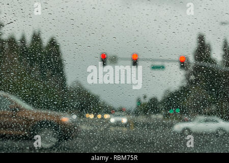 Le gocce di pioggia sul parabrezza in un giorno di pioggia, traffico sfondo luminoso, California Foto Stock