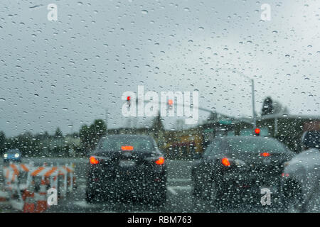 Le gocce di pioggia sul parabrezza in un giorno di pioggia, traffico sfondo luminoso, California Foto Stock