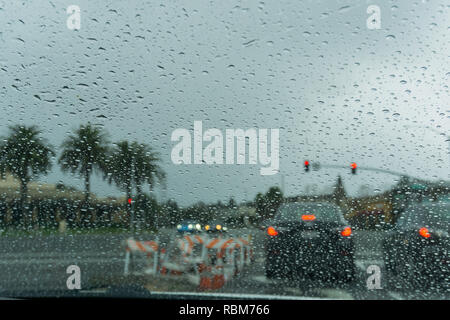 Le gocce di pioggia sul parabrezza in un giorno di pioggia, traffico sfondo luminoso, California Foto Stock