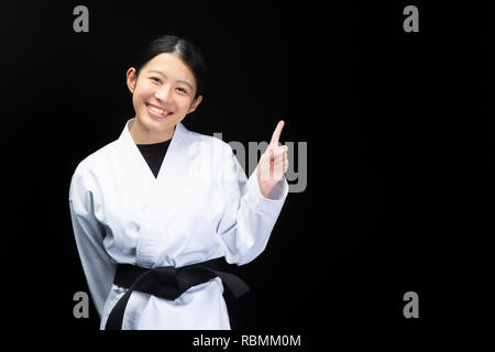 La donna in un abito di karate rivolto con le dita su sfondo nero Foto Stock